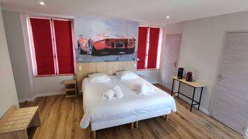 Een hotelkamer met een bed, een houten vloer, een schilderij van een rode auto, een rood gordijn en een koffieapparaat.