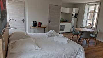A hotel room with a bed, a small table with a coffee maker, a kitchenette, and a dining area with chairs.
