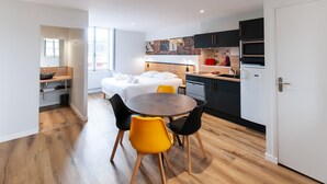A modern hotel room with a bed, a small kitchen area, and a dining table with chairs. - Malicorn' Appart-hôtel (Malicorne-sur-Sarthe)