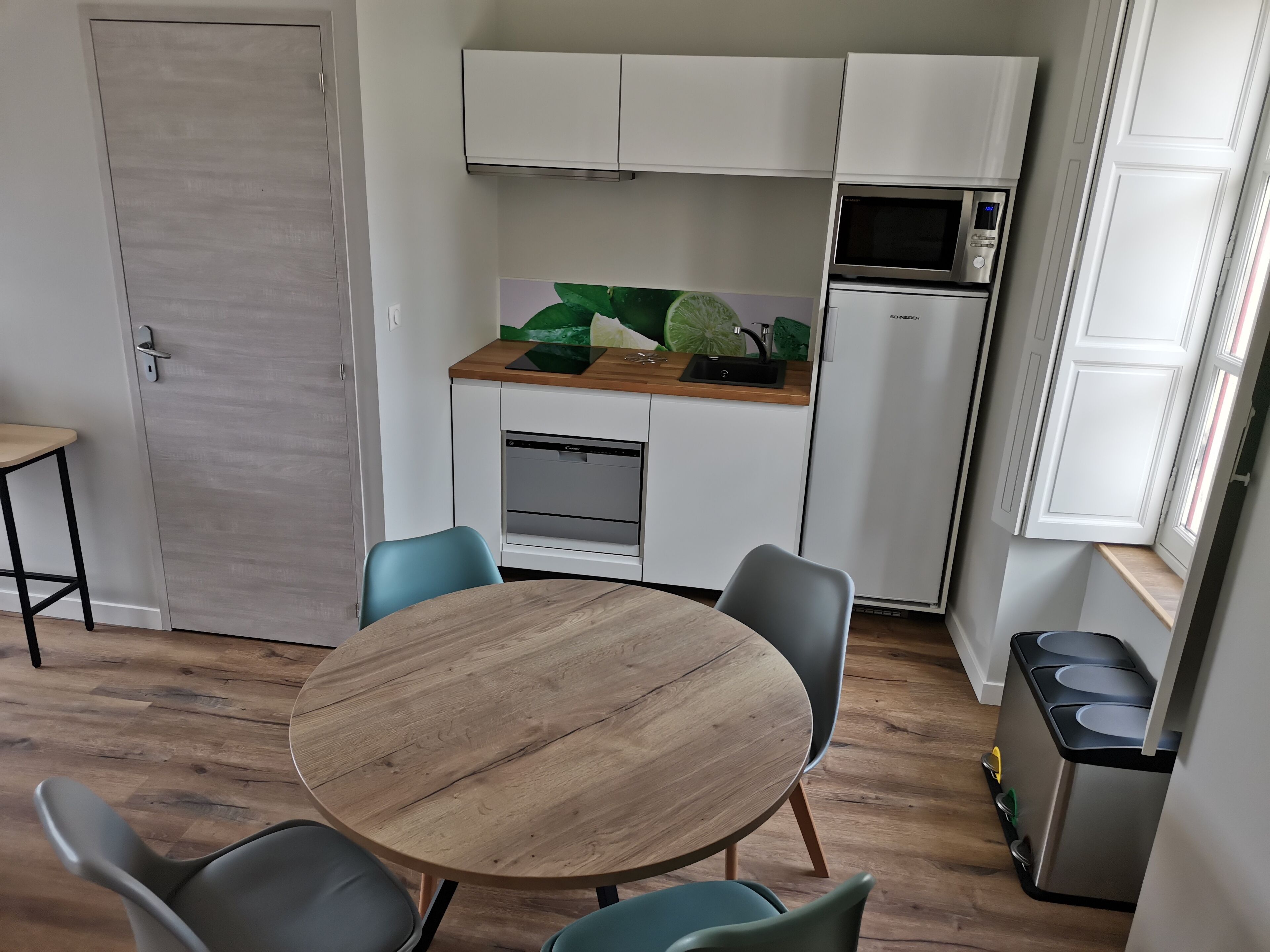 Cocina compacta con zona de comedor, que incluye una mesa redonda de madera y sillas, un microondas y un lavamanos.