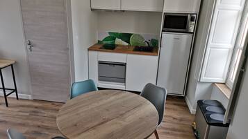 Cocina compacta con zona de comedor, que incluye una mesa redonda de madera y sillas, un microondas y un lavamanos.