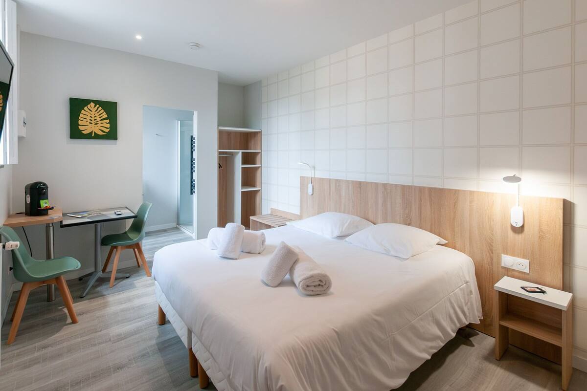 A hotel room with a bed, a desk, a chair, a wardrobe, and a shower area.