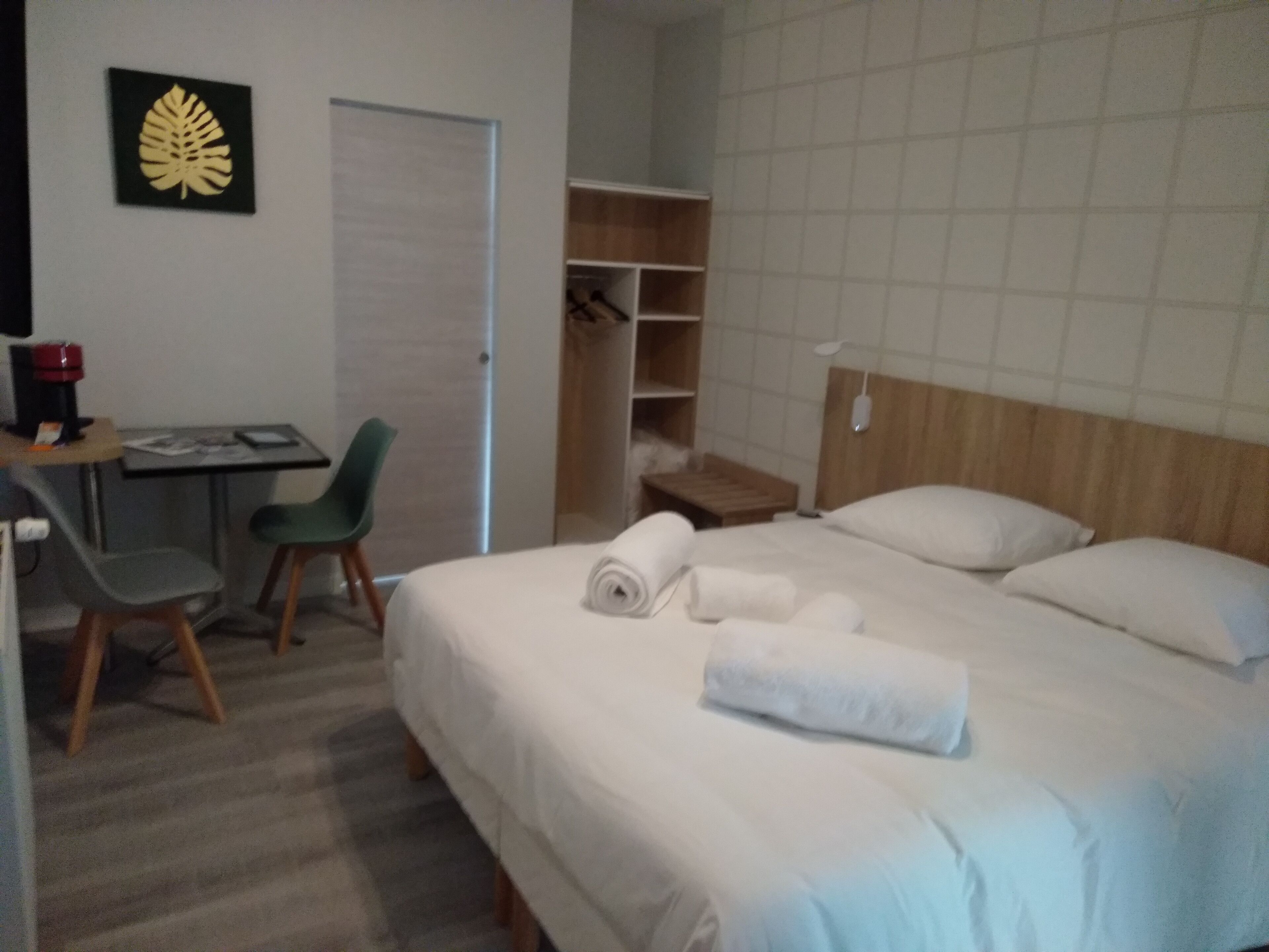 Habitación de hotel con cama, escritorio con silla, armario y pequeña mesa con cafetera.