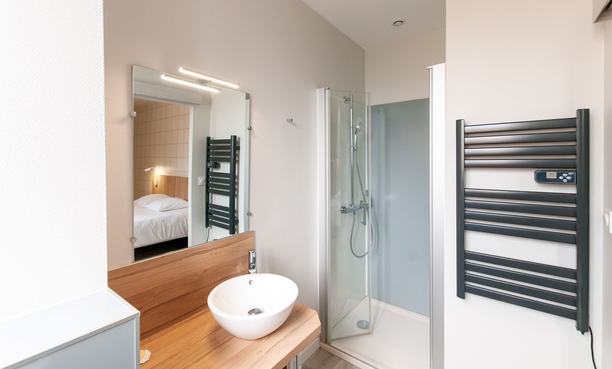 A modern bathroom with a wooden vanity, a white sink, a glass shower enclosure, and a towel rack.