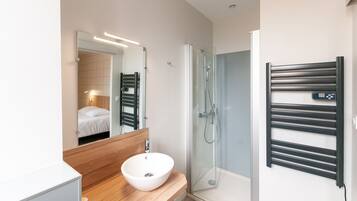A modern bathroom with a wooden vanity, a white sink, a glass shower enclosure, and a towel rack.