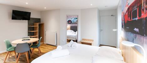 A hotel room with a bed, a desk with chairs, a TV, a radiator, and a door.