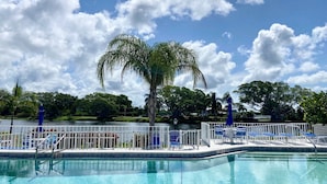 Une piscine d’un bleu éclatant, avec un palmier au centre, entourée de chaises longues et d’une clôture blanche.