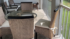Une terrasse ensoleillée, dotée de meubles en osier, d’une table en verre et d’un ventilateur de plafond.