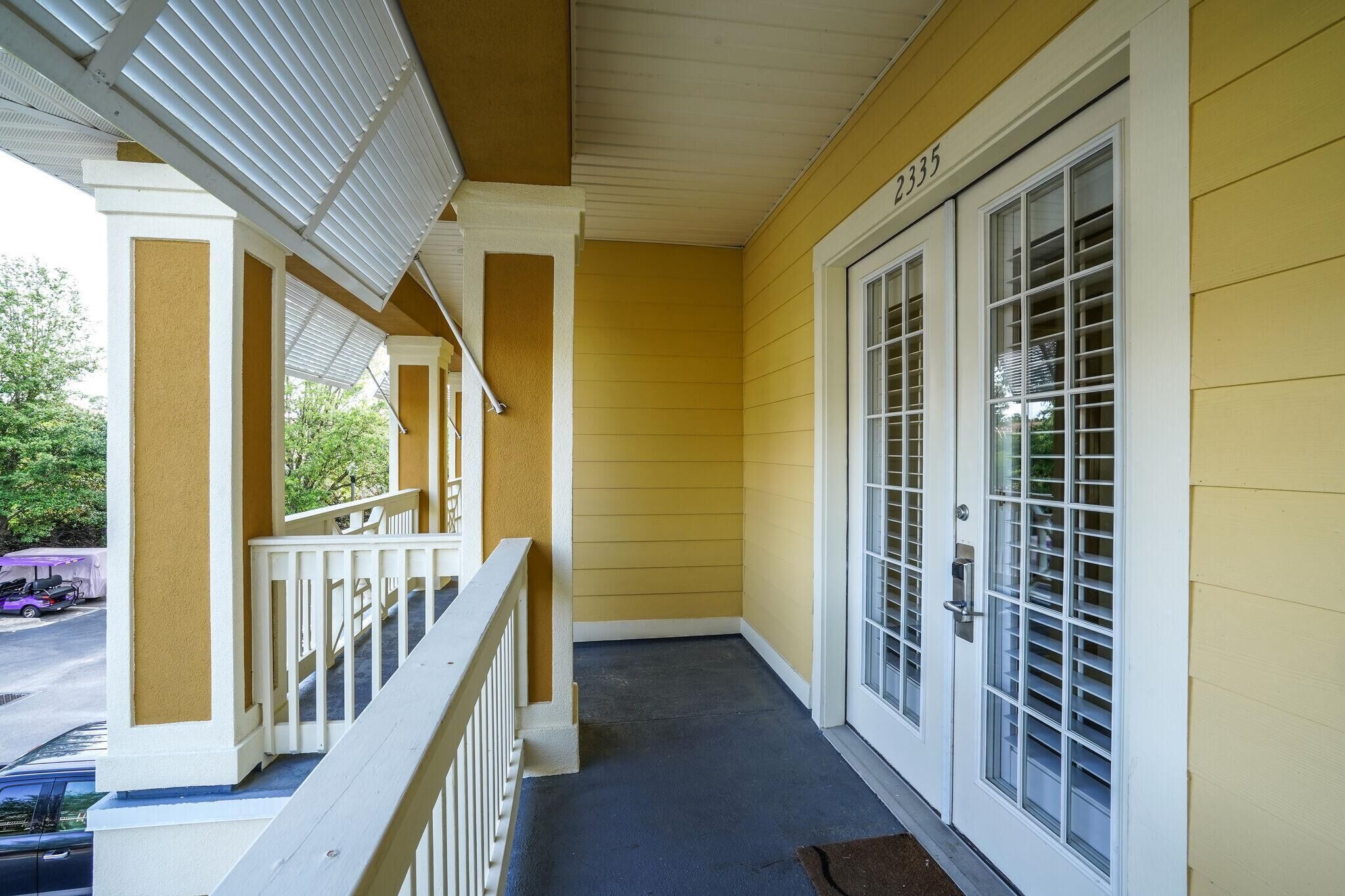 A covered porch with a white railing, yellow siding, and a door with a window.