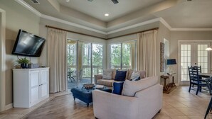 A spacious living room with a large TV, a sofa, and a dining area with chairs. - Chic 1BR/1BA Retreat with Serene Balcony Views and Golf Cart at Sandestin Golf and Beach Resort! (Miramar Beach)
