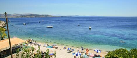 Ein Strand mit klarem, blauem Wasser, Booten und Sonnenschirmen.