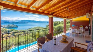 A covered outdoor area with a table set for dining, overlooking a scenic view of a lake and mountains. - Bougainvillea Large Private Pool Walk to Beach Sea Views A C Wifi Car Not Required Eco-friend - 195 (Corfu)