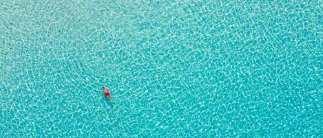 A clear turquoise pool with a person in a red swimsuit floating.