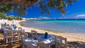 An outdoor dining area with white tables and chairs, overlooking a clear blue sea with boats and a distant shoreline. - Dinos Walk to Beach Sea Views A C Wifi Car Not Required - 291 (Corfu)