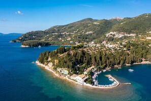 Vue aérienne d’une zone côtière comprenant un port de plaisance, des collines densément boisées et quelques bâtiments dispersés.