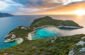 Un paysage côtier offrant une vue dégagée sur des eaux turquoise, des collines verdoyantes et un coucher de soleil.