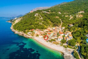 Vue aérienne d’une ville côtière avec des bâtiments construits sur une colline, une plage et des eaux d’un bleu limpide.