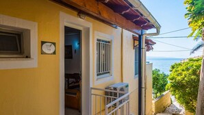 Ein gelbes Gebäude mit Balkon und Meerblick, eine Tür zu einem Innenraum sowie eine kleine Klimaanlage an der Außenwand.