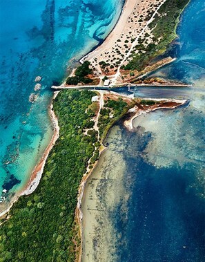 Luchtbeeld van een kustgebied met een strand, dichte groene begroeiing en helderblauw water.