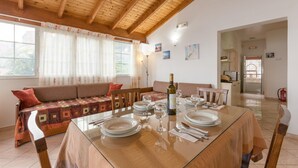 Een eetgedeelte met een glazen tafel voor vier personen, een bank met gekleurde kussens, en een houten plafond.
