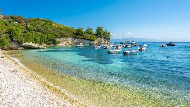A beach with clear shallow waters, rocky shore, and boats anchored near the shore. - Spiros Jetty House Walk to Beach Sea Views A C Car Not Required - 302 (Paxos)