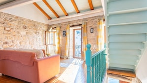 A cozy room with a stone wall, wooden beams, a pink sofa, and a teal staircase. - Spiros Jetty House Walk to Beach Sea Views A C Car Not Required - 302 (Paxos)