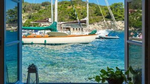 A view from a window of a boat docked at a marina with clear blue water and a hilly landscape in the background. - Spiros Jetty House Walk to Beach Sea Views A C Car Not Required - 302 (Paxos)