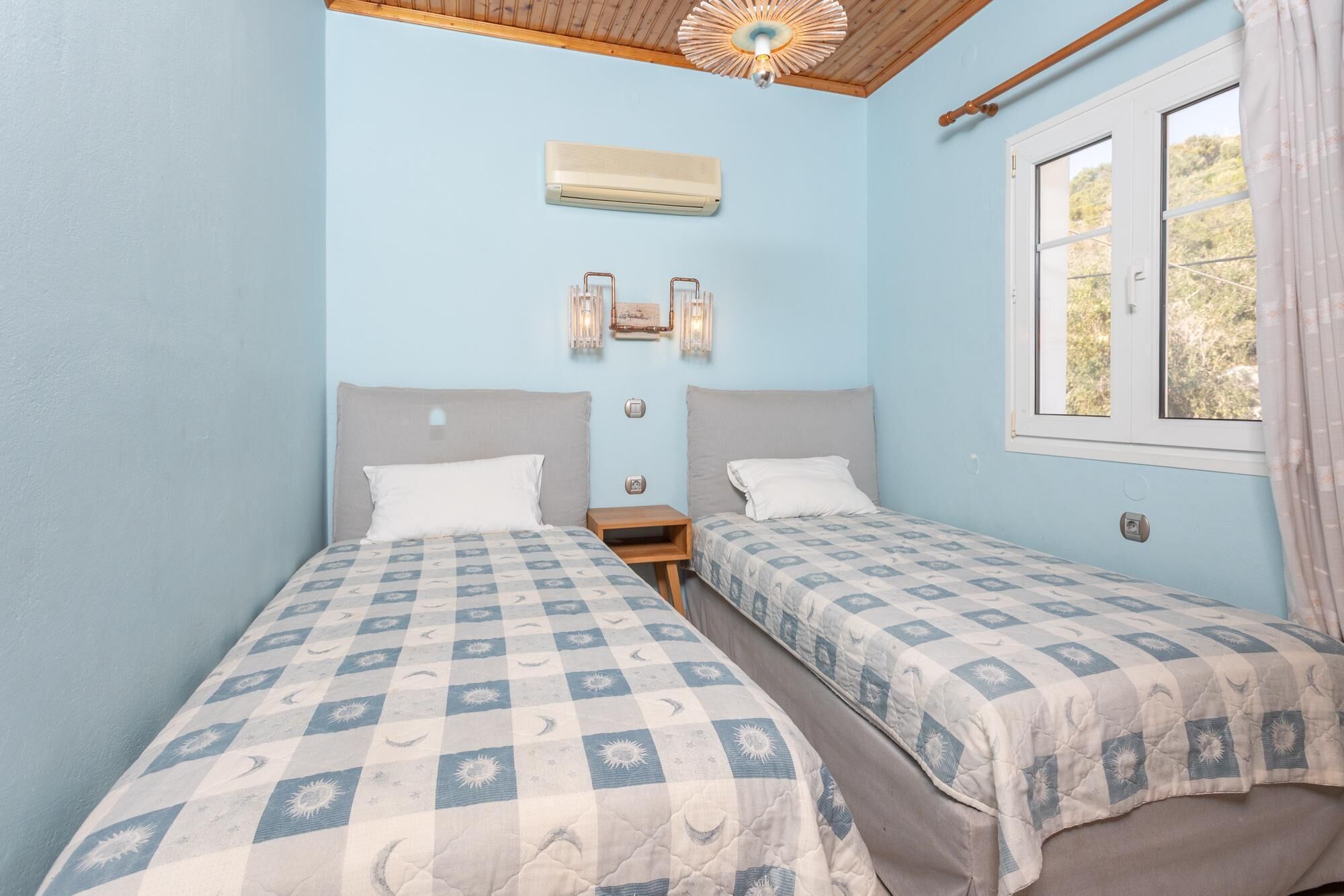 A bedroom with two beds, a window, an air conditioning unit, and wall-mounted lights.