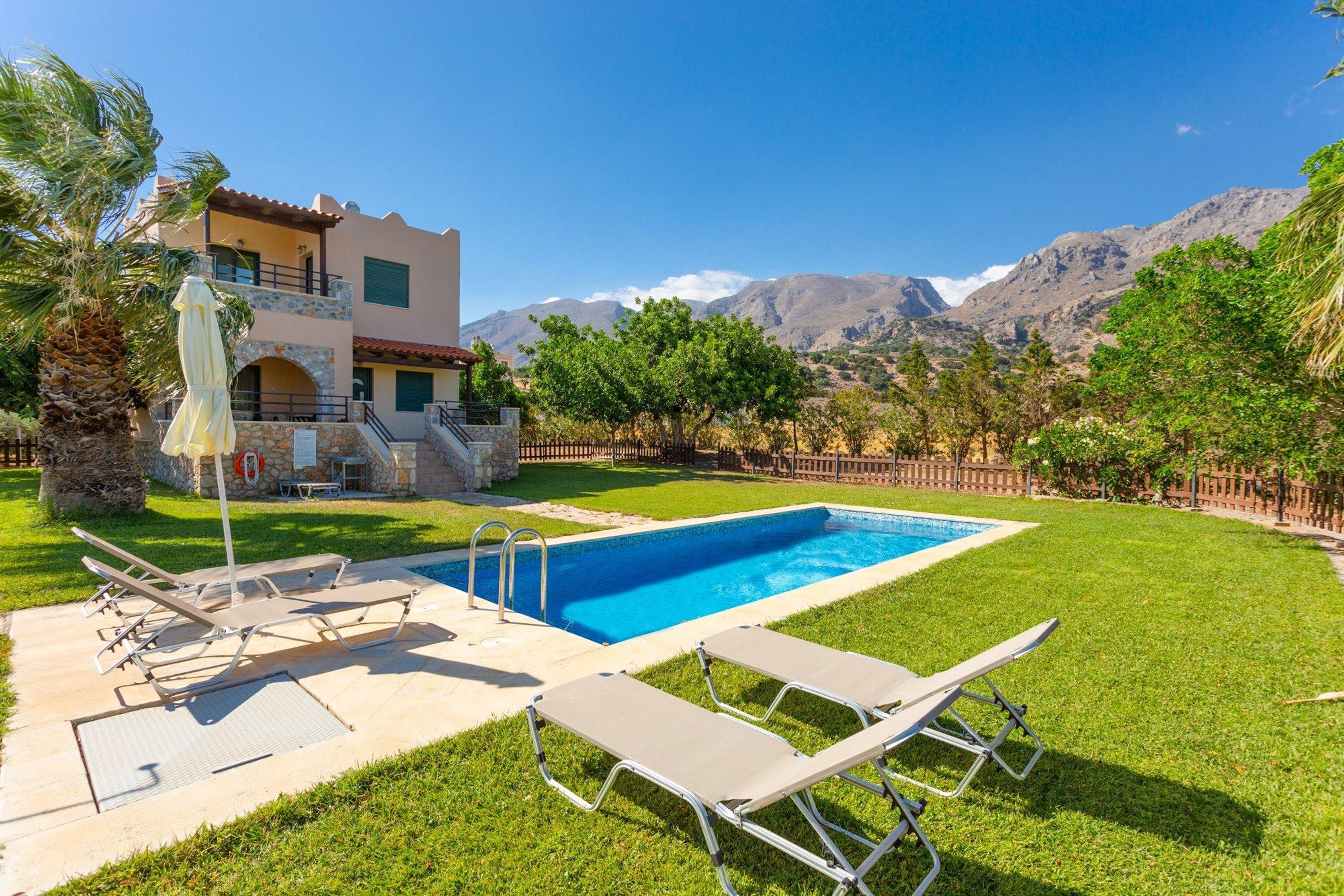 A pool area with lounge chairs, a stone building, and mountains in the background.