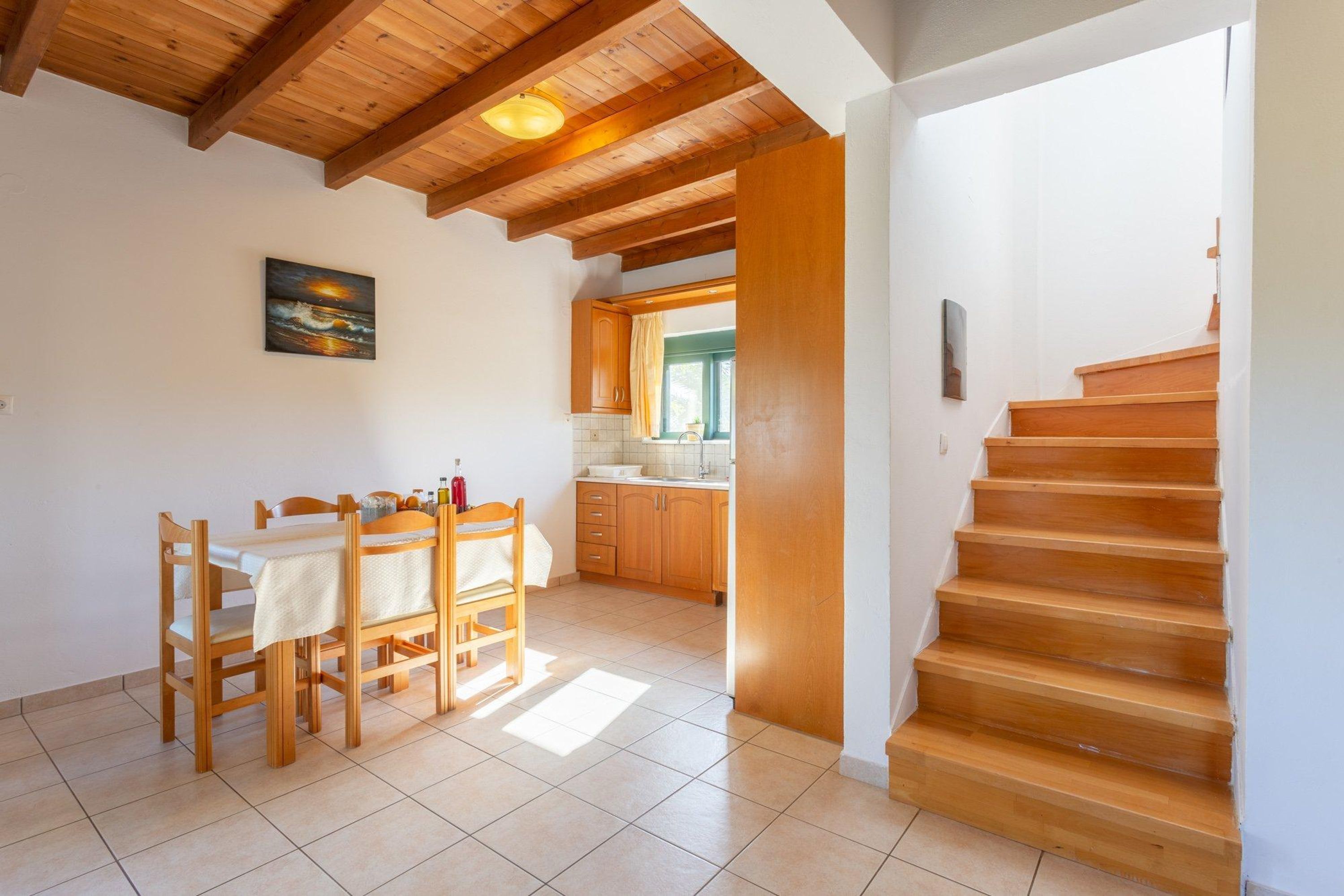A dining area with a wooden table and chairs, a kitchen with wooden cabinets, and a wooden staircase.