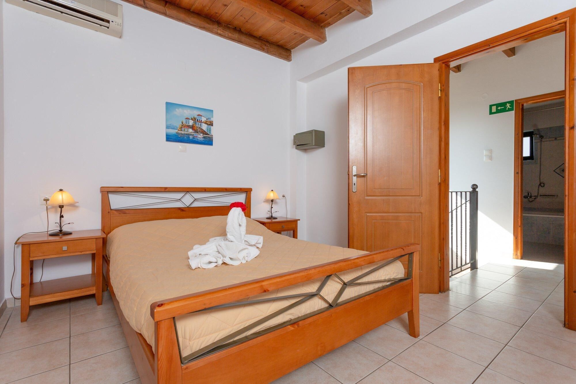A hotel room with a wooden bed, two bedside tables with lamps, a painting on the wall, and a wooden door.