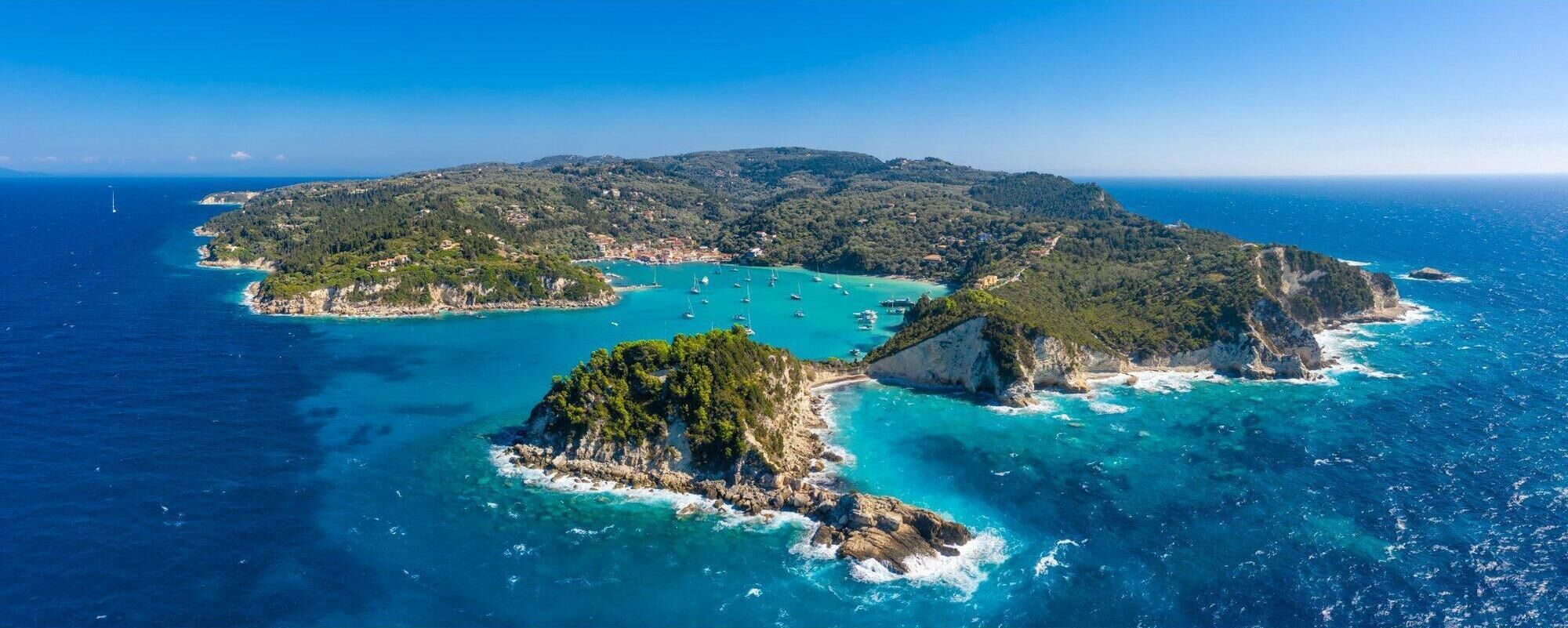 Luchtbeeld van een kusteiland met helder turquoise water, rotsachtige uitsteeksels en dichte groene begroeiing.