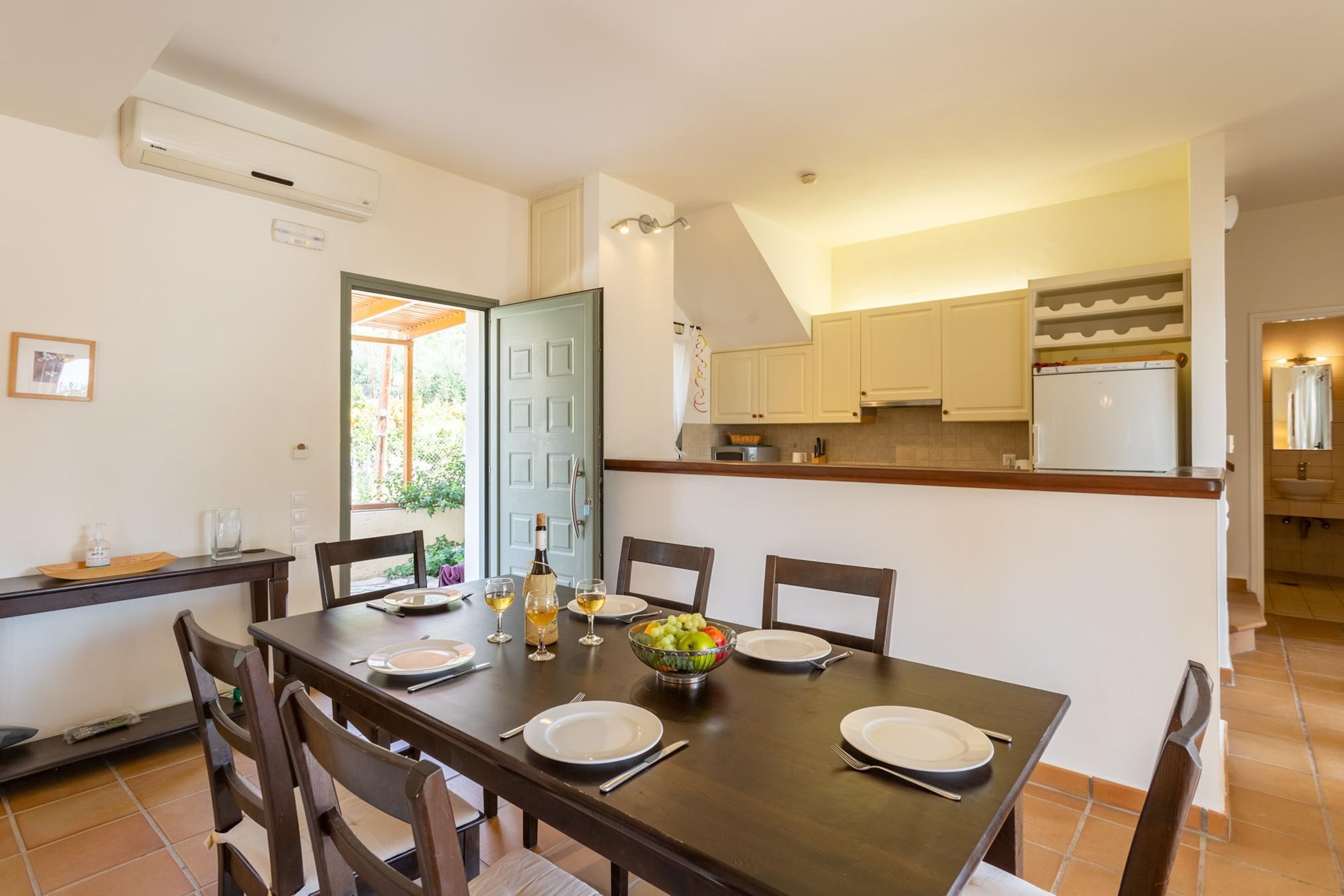 A dining area with a table set for four, a kitchen in the background, and a door leading outside.