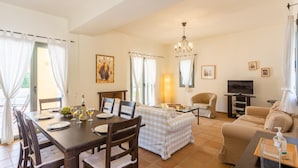 A dining area with a table set for four, a sofa, a TV, and a chandelier. - Villa Katerina Large Private Pool Walk to Beach Sea Views A C Wifi Car Not Required - 1021 (Kefalonia)