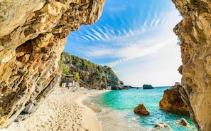A coastal beach with rocky cliffs, clear turquoise waters, and a small building with steps leading down to the beach. - Villa Youla Large Private Pool Walk to Beach Sea Views A C Wifi Car Not Required - 1025 (Corfu)
