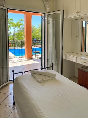 A hotel room with a bed, a desk, and a view of a swimming pool and outdoor area. - Villa Youla Large Private Pool Walk to Beach Sea Views A C Wifi Car Not Required - 1025 (Corfu)