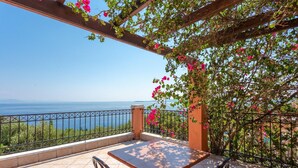 Une terrasse avec une table et des chaises, offrant une vue panoramique sur la mer et les collines.