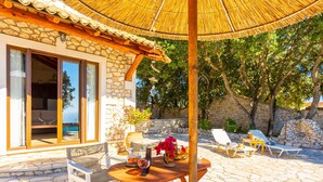Un edificio de piedra con una pérgola de madera, asientos al aire libre y vistas al mar.