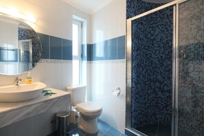 A bathroom with a white sink, a toilet, and a glass shower enclosure with blue mosaic tiles.
