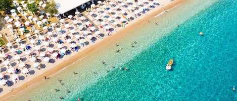 An aerial view of a beach with numerous umbrellas and people.