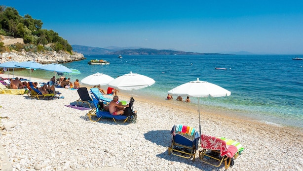 A beach with people sunbathing under umbrellas, clear blue water, and boats in the distance. - Villa Petros Large Private Pool Walk to Beach Sea Views A C Wifi Car Not Required - 180 (Corfu)