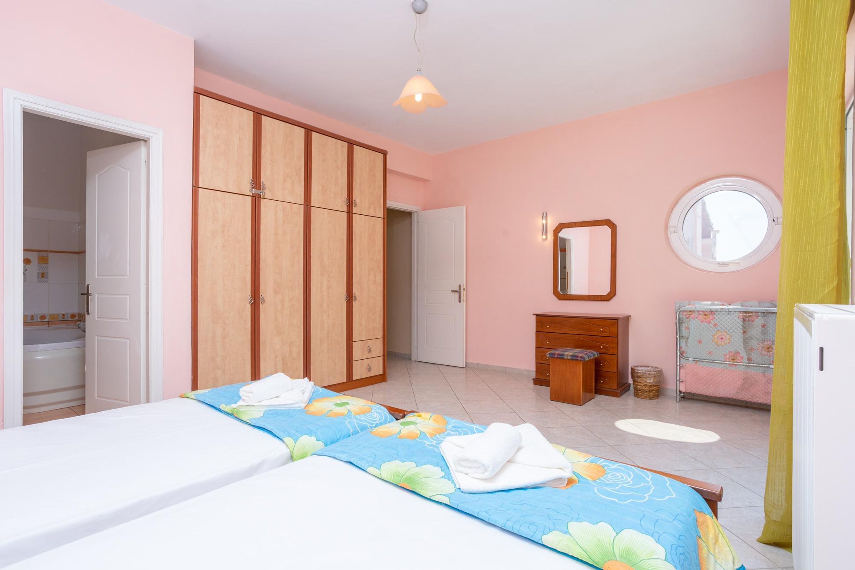 Un dormitorio con cama, armario, cómoda y espejo, además de una ventana.