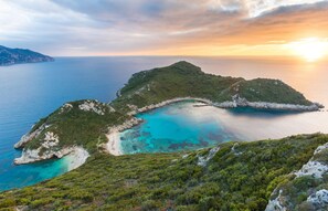 A coastal landscape with a small island, clear turquoise waters, and a sunset.
