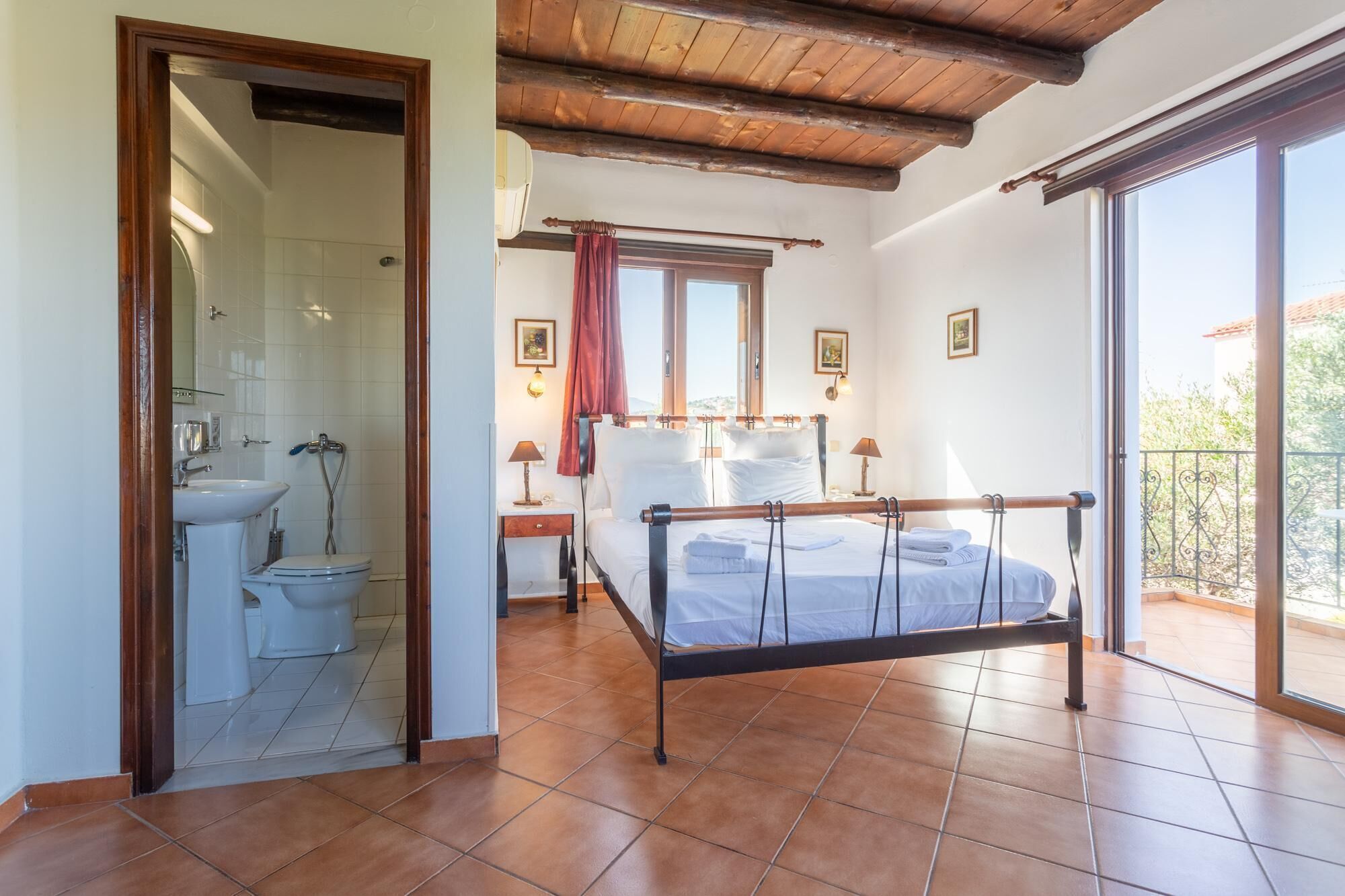 Un dormitorio con cama, un baño con inodoro y lavamanos, y un balcón con barandilla.