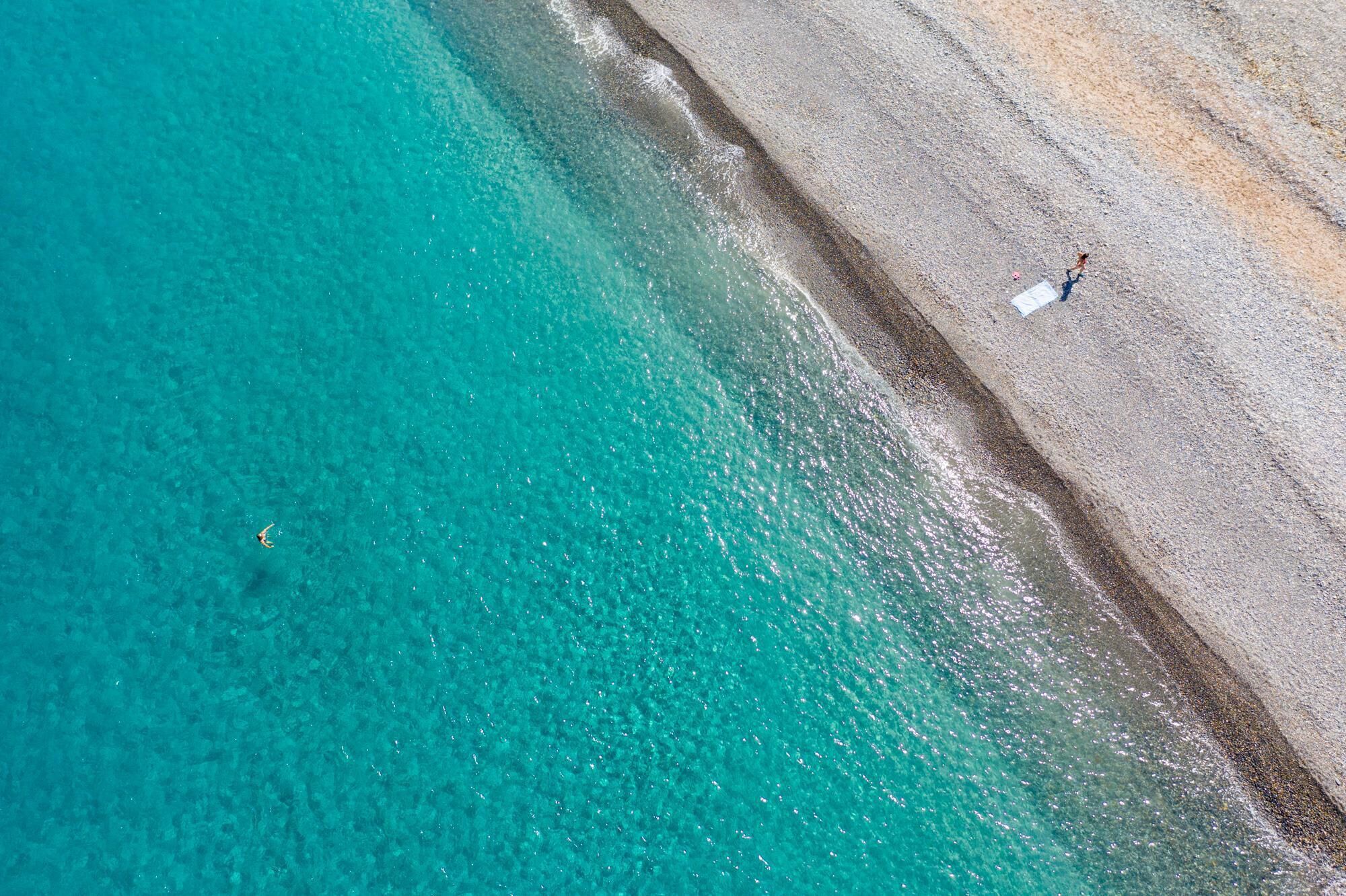 An aerial view of a beach with clear turquoise water and a sandy shore.