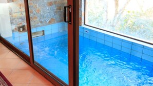 Una piscina con agua azul cristalina, un muro de piedra y suelo de baldosas.