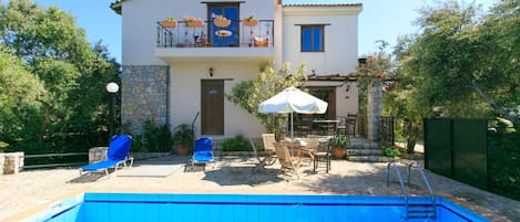 A two-story house with a swimming pool, outdoor seating, and a garden.