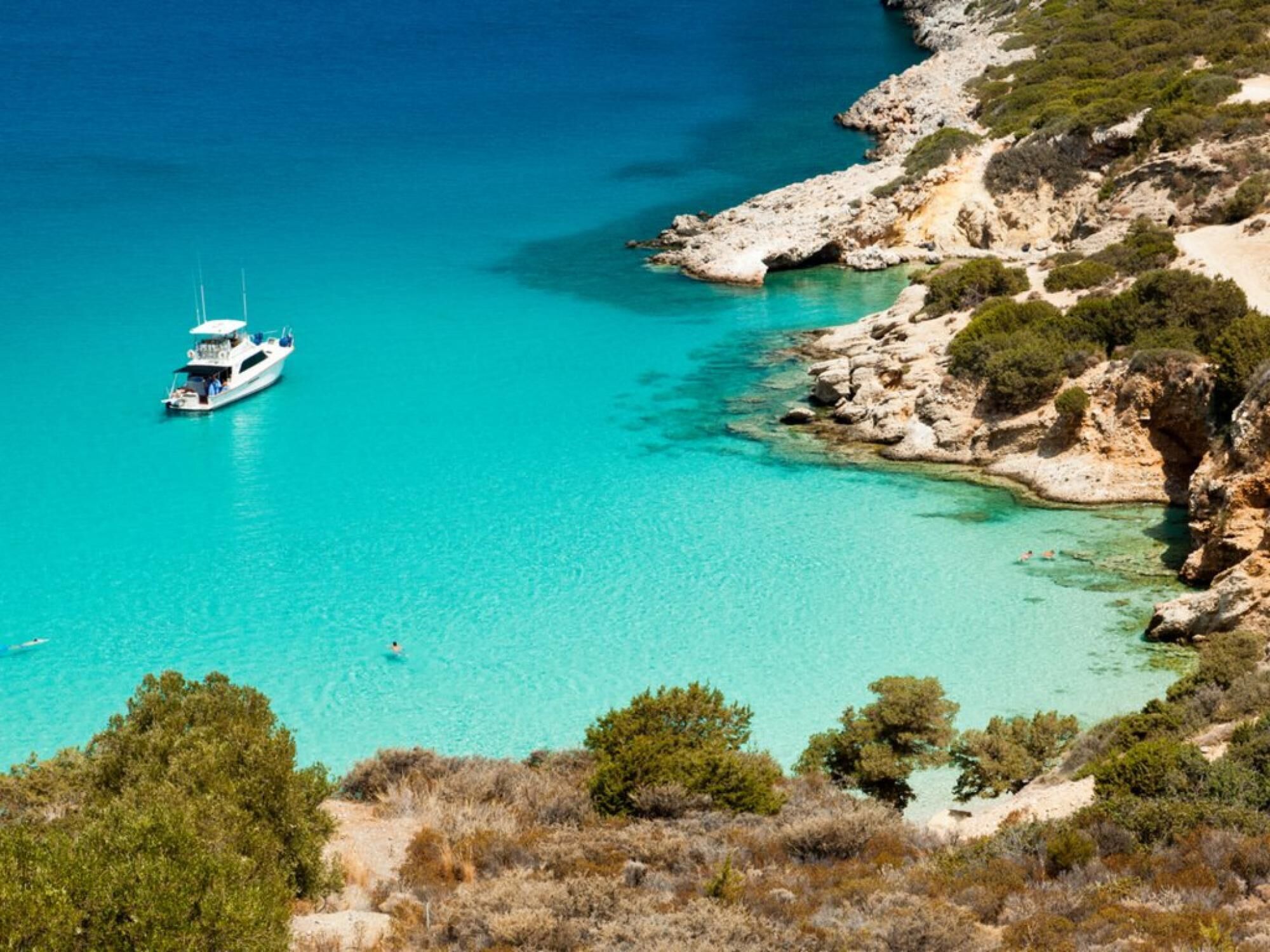 A boat on clear turquoise waters near rocky terrain with sparse vegetation.