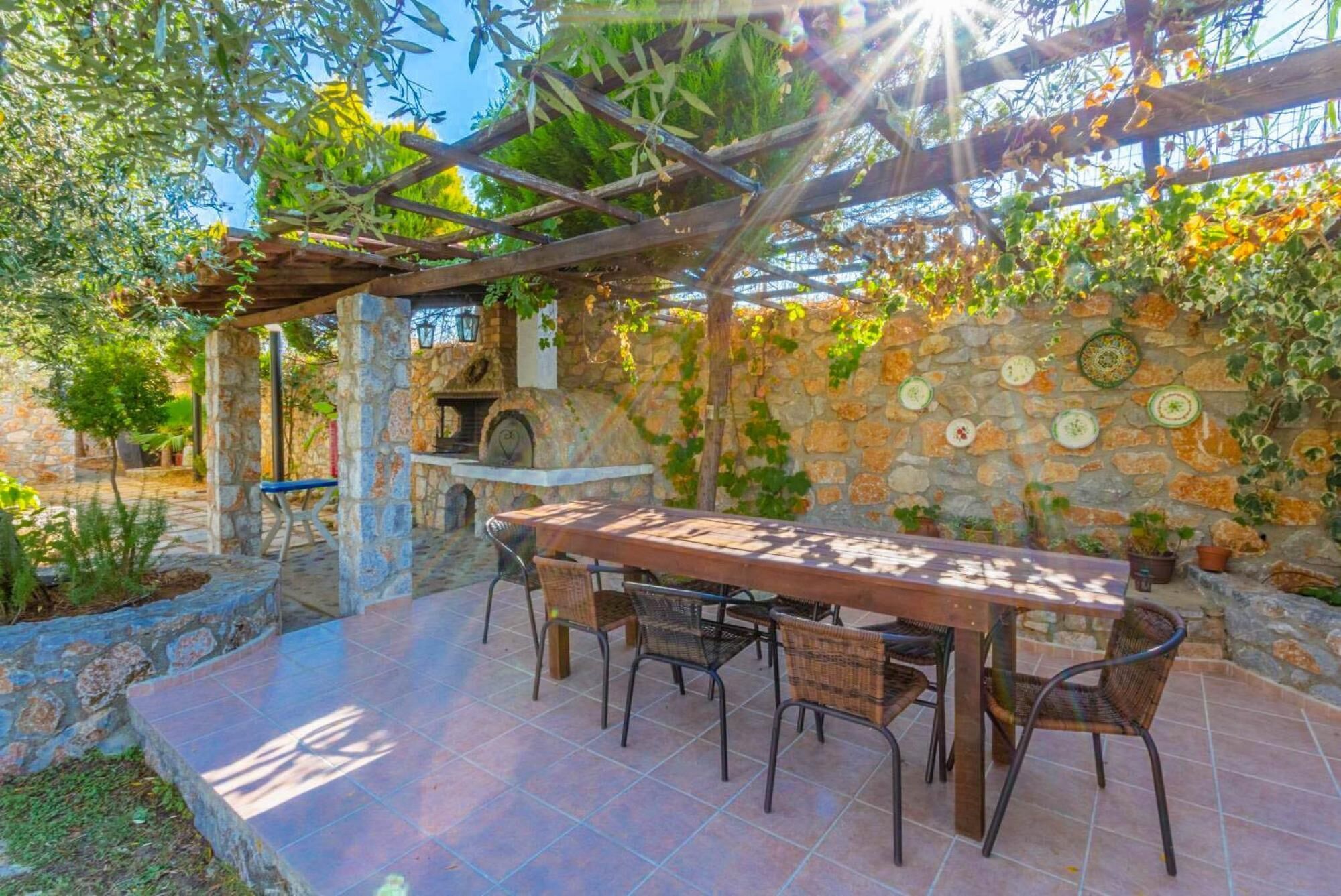 Eine Terrasse im Freien mit einer Steinsäule, einer Pergola und einem langen Holztisch mit Stühlen.