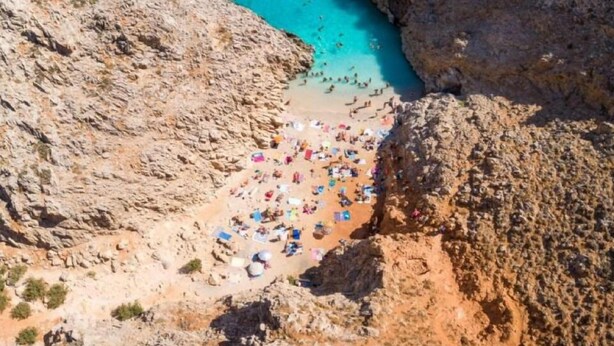 Eine Küstenklippe mit Strand, Sonnenschirmen und Menschen.
